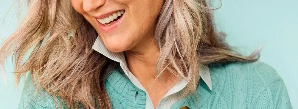 Close up of a woman smiling, wearing a misty aqua sweater.